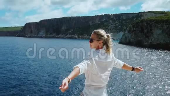 穿着白色衣服的女人在蓝色的大海前举起武器在暑假期间享受自由在希腊旅行视频的预览图