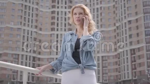 在摩天大楼前用手机说话的可爱微笑自信的金发女人的肖像城市生活方式女性城市视频的预览图
