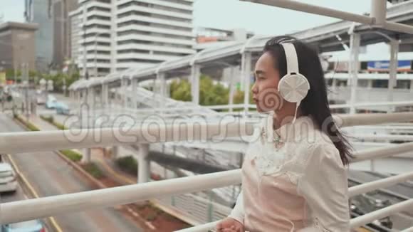 一个悲伤的印尼女孩穿着白色耳机穿过市中心的过渡听音乐视频的预览图