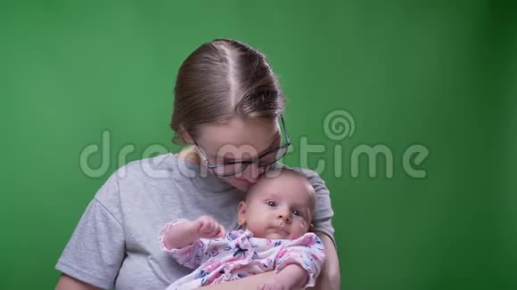 漂亮母亲在绿色背景下亲吻她可爱美丽的新生女儿的特写肖像视频的预览图