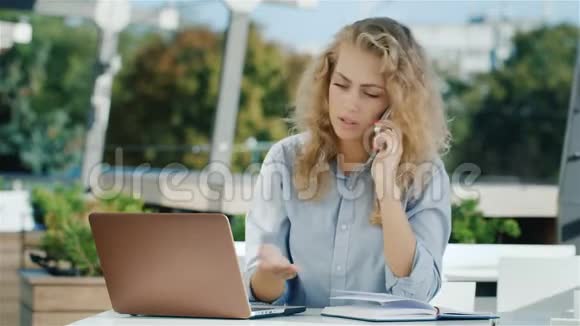 很忙的商务女性它与笔记本电脑一起工作手机看笔记本上的录音视频的预览图
