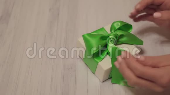 女士双手解开白色礼盒上的绿色丝带在轻木器上打开的女性手的锁闭镜头视频的预览图