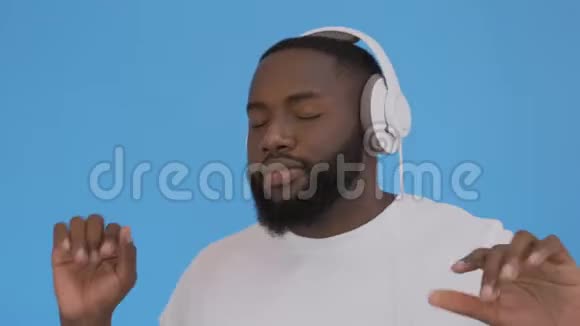 非裔美国人用耳机听音乐而不是孤立的蓝色背景快乐的脸视频的预览图