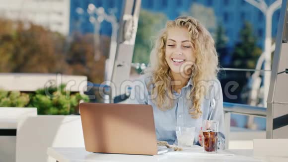 年轻的商务女性在一家带笔记本电脑的咖啡馆工作吃冰淇淋在一家咖啡馆的夏日露台上视频的预览图