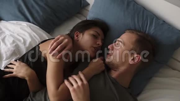 年轻的白种人相爱的夫妇在床上聊天和亲吻早上醒来迷人的男人的俯视图视频的预览图
