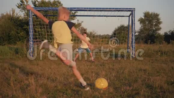 两个男孩在日落时踢足球一个足球正在击球足球进球孩子们胜利的梦想视频的预览图