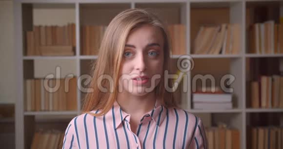 在大学图书馆里一位年轻漂亮的白种人女学生看着镜头带着羞怯的微笑特写视频的预览图