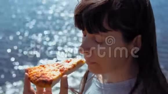 女孩咬掉一块比萨饼然后在大海的背景下咀嚼它视频的预览图