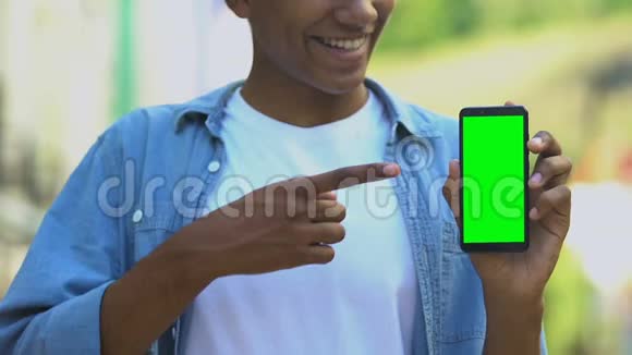 微笑着用绿色屏幕指着智能手机的黑人少年视频的预览图