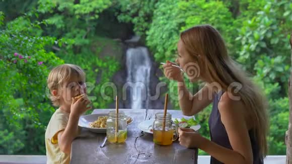 年轻的女人和她的小儿子在咖啡馆里有一个兰奇在峡谷和瀑布上有一个史诗般的景色前往巴厘岛视频的预览图
