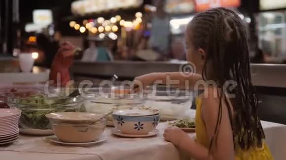 餐馆里有各种蔬菜的桌子小女孩把食物放在盘子里4K视频的预览图