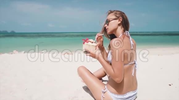 在阳光明媚的日子里坐在沙滩上喝椰子的女人视频的预览图