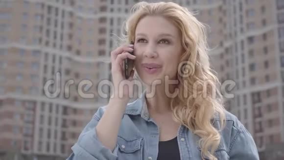 在摩天大楼前用手机说话的漂亮微笑自信的金发女人的特写镜头城市生活方式视频的预览图