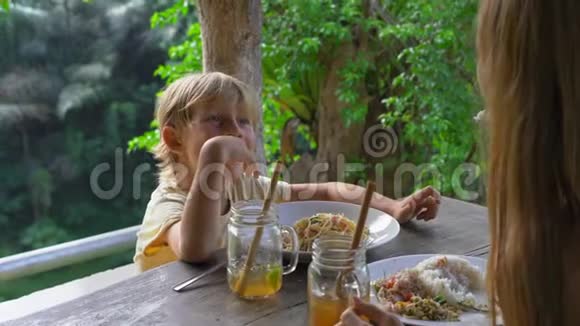 年轻的女人和她的小儿子在咖啡馆里有一个兰奇在峡谷和瀑布上有一个史诗般的景色前往巴厘岛视频的预览图
