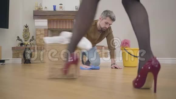 英俊的白人年轻人洗地板美丽的女腿在优雅的红色高跟鞋的前景视频的预览图
