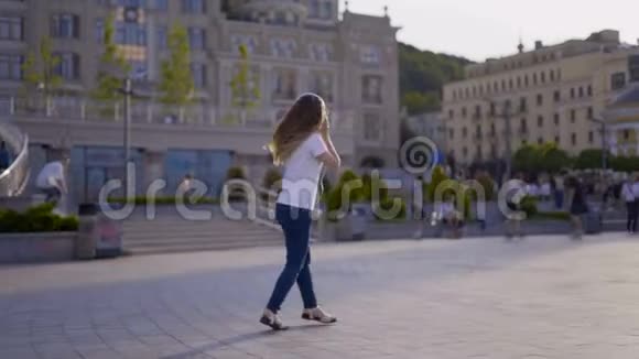 有趣的年轻女孩在城里散步跳舞很有趣穿着大白耳机听音乐的女人视频的预览图