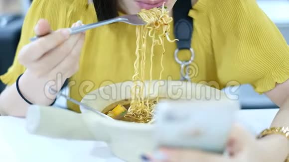 女孩在吃饭前呼吸着热面条同时使用智能手机听着人们在食物法庭上的声音视频的预览图