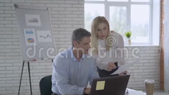 男人坐在办公室的椅子上年轻的女人站在附近两人都看着桌子上的一张纸主任视频的预览图