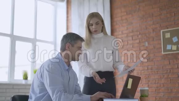 男人坐在办公室的椅子上年轻的女人站在附近两人都看着桌子上的一张纸主任视频的预览图