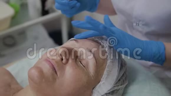 专业美容师将血清应用于美容院老年妇女的面部视频的预览图