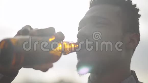 一个英俊的非裔美国人在户外对着镜头喝啤酒阳光明媚的天空视频的预览图