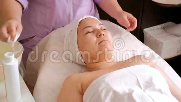 一位专业的女性美容师用湿棉垫擦客户的脖子和领口在美容院的亚洲女孩视频的预览图