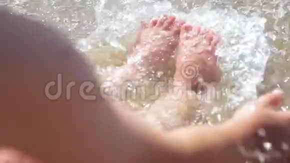 一个男孩坐在海边捕捉海浪海浪冲刷着男孩脚有孩子的家庭的海上假期视频的预览图