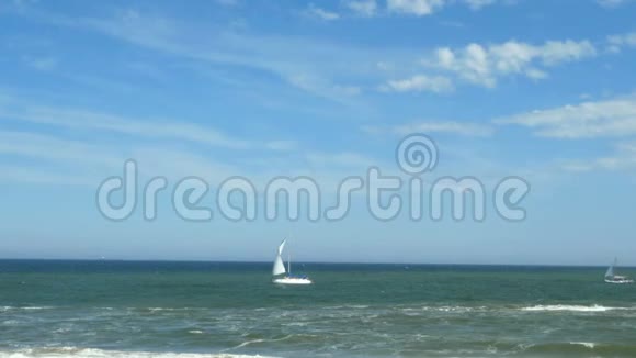 帆船在海面上晴朗的天气天空上有几片白云背景帆船在靠近海岸的蓝海中航行视频的预览图