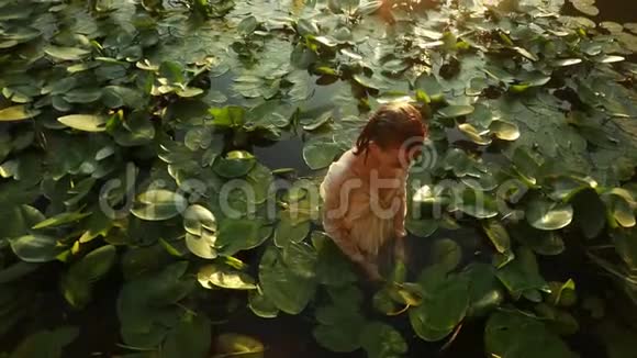 年轻女子在湖里沐浴着黄色的水的叶子视频的预览图
