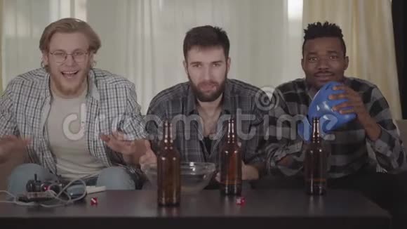 两个高加索人和一个非裔美国人在家休息在电视上看拳击啤酒瓶空的视频的预览图