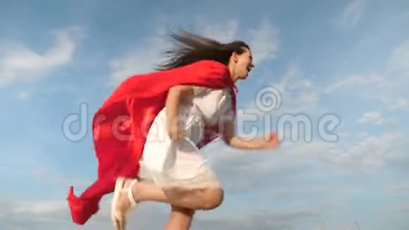 快乐的超级英雄女孩穿着红色斗篷跑着笑斗篷在风中飘扬开朗的年轻女人扮演超级英雄视频的预览图