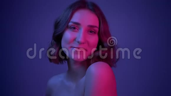 拍摄特写镜头年轻漂亮的女性微笑着摆在镜头前她的头发飘着霓虹灯蓝色视频的预览图