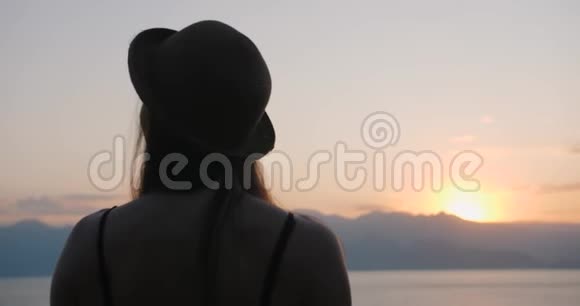 戴帽子的女人看日落时的海景在自然中放松享受下午的宁静和平静的景观自然视频的预览图