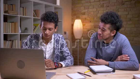 非洲裔美国和印度男性学生的特写镜头讨论一个项目一起使用笔记本电脑和采取视频的预览图