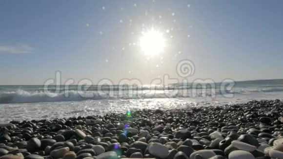 海浪冲刷着鹅卵石海滩迎着灿烂的阳光眺望视频的预览图