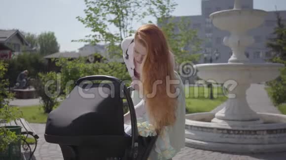 美丽的红发女人弯下腰在公园里微笑这位女士和她的孩子一起享受阳光明媚的一天视频的预览图