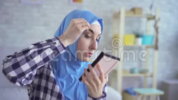 美丽的年轻穆斯林妇女化妆照顾皮肤照镜子视频的预览图