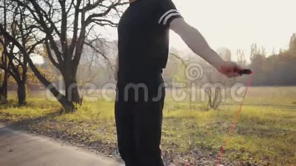 年轻的白种人男孩穿着黑色运动服在日落时在秋天的公园里跳绳户外强壮运动员训练视频的预览图
