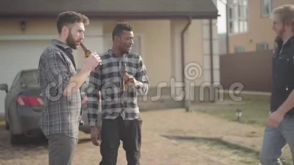 两个白人和非裔美国人站在大房子前喝啤酒第三个朋友来了男人问候视频的预览图