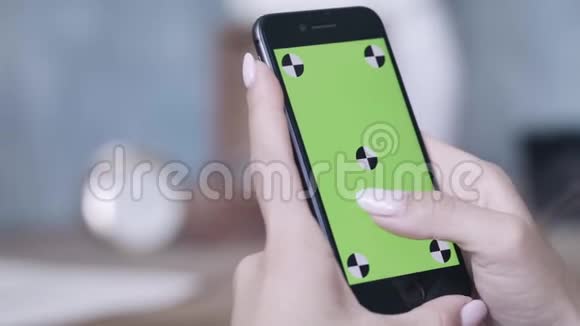 年轻女性的双手完美的美甲手握智能手机并在彩色键绿色屏幕上滑动视频的预览图