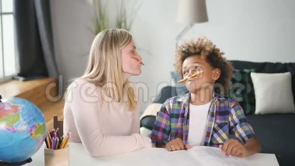 快乐的女人和有趣的男孩坐在桌子旁用铅笔在周围闲逛视频的预览图