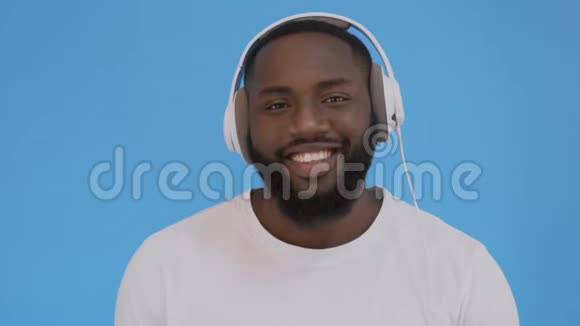 非裔美国人用耳机听音乐而不是孤立的蓝色背景快乐的脸视频的预览图