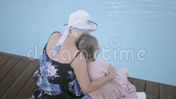 后景小滑稽女孩扎着辫子成熟的女人坐在池边休息和休闲视频的预览图