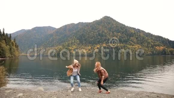 两个女孩在湖上跳着在山的背景下跳舞为博客而笑社交媒体旅游视频的预览图