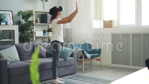 穿休闲服装的苗条的年轻女士使用增强现实眼镜站在家里的灯光室里双手移动视频的预览图