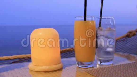 在岸边的一张桌子上的一个酒吧里站着两只玻璃杯里面有鸡尾酒和一支燃烧的蜡烛视频的预览图