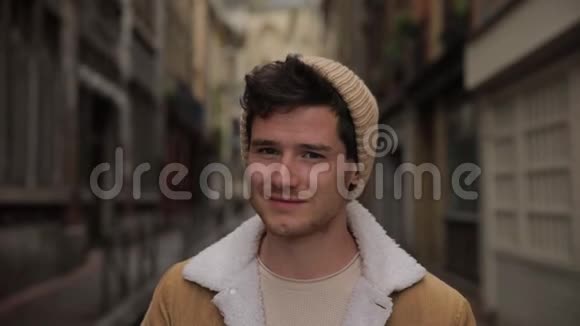 一位年轻时尚的帅哥在欧洲一个古老城镇的街道上对着镜头微笑的肖像慢动作视频的预览图