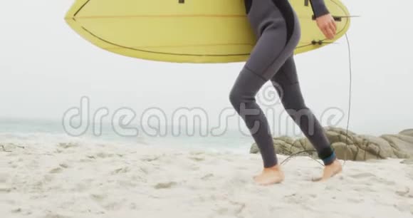 白种人女性冲浪者在海滩上用冲浪板跑步的侧视图视频的预览图