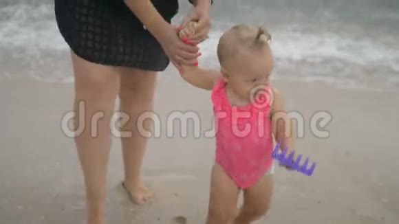 一个穿着粉红色泳衣的小女孩和她妈妈在海滩上视频的预览图