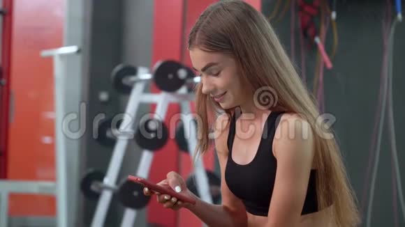 经过强化训练后美丽的少女在长凳上休息时微笑着使用智能手机视频的预览图